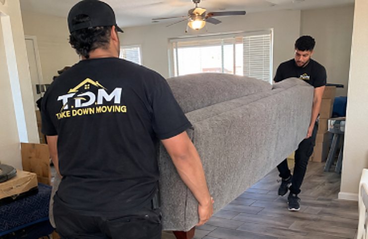 Two T.D.M movers in black TDM shirts carrying a couch